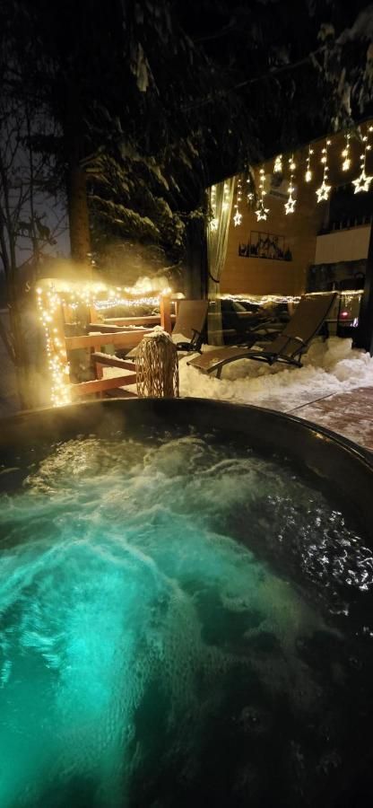 Podświetlona woda w jacuzzi nocą, w tle lampki i taras w śniegu