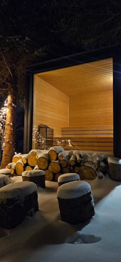 Podświetlona sauna nocą, przed nią drewno i pieńki w śniegu