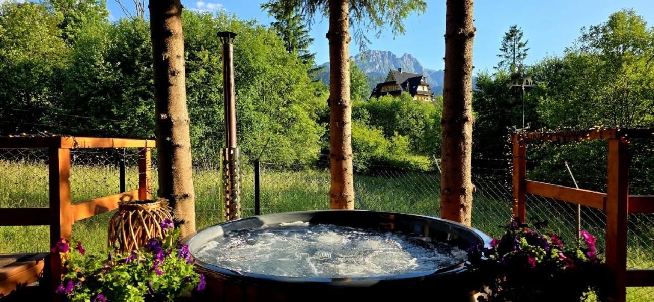 Bąbelki w jacuzzi, za drzewami góry i dom w stylu zakopiańskim